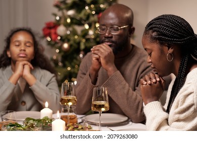 Young African woman, her husband and their cute daughter praying before dinner with their hands put together by chin - Powered by Shutterstock