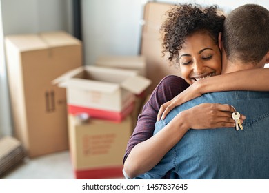 Young african woman holding home keys while hugging boyfriend in their new apartment after buying real estate. Lovely girl holding keys from new home and embracing man. Couple around cardboard boxes. - Shutterstock ID 1457837645