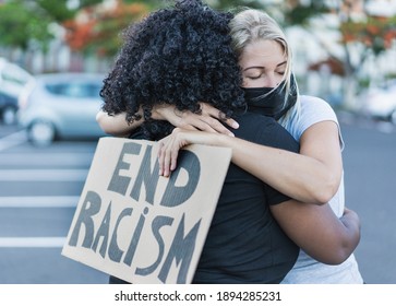 Young african woman hugging a caucasian woman after a protest - Northern woman with end racism bannner in her hands - Concept of no racism