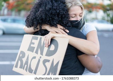 Young african woman hugging a white northern woman after a protest - Northern woman with end racism bannner in her hands - Concept of no racism  - Powered by Shutterstock