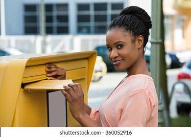 Young African Woman Inserting Letter In Mailbox