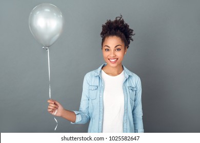 Young african woman isolated on grey wall studio casual daily lifestyle holding balloon