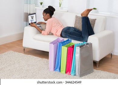 Young African Woman Lying On Sofa Shopping Online On Laptop