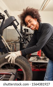 Young African Woman As A Mechanic Apprentice With Car Tires In The Car Workshop