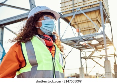 A young African woman mine worker wearing protective wear is looking off camera while wearing a covid 19 face mask with coal mine equipment in the background