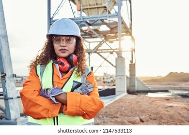 A young African woman mine worker wearing protective wear is looking at the camera with coal mine equipment in the background