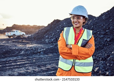 A young African woman mine worker wearing protective wear is looking off camera with coal mine equipment in the background - Shutterstock ID 2147533133