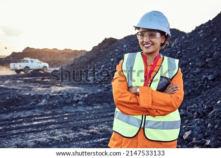 A young African woman mine worker wearing protective wear is looking off camera with coal mine equipment in the background