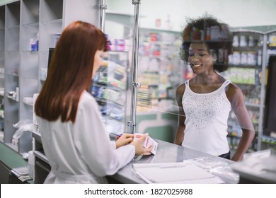 Young African Woman Patient Buying Medicines In Pharmacy. Back Angle View Of Smiling Woman Pharmacist Giving Box With Drug To Black Woman In Drugstore