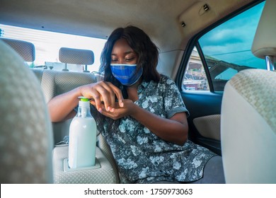 A young African woman pressing on a hand sanitizer and wearing a locally made face mask for protection in a passenger seat of a car.