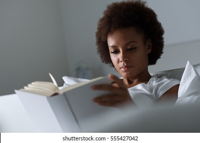 Young african woman relaxing at home and reading a book, she is lying on the bed
