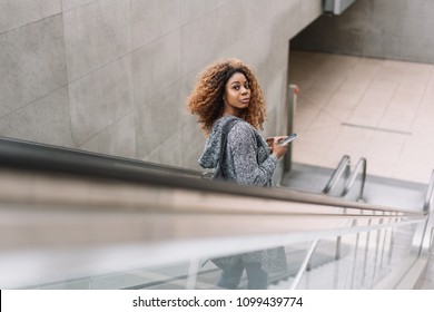 Young African Woman Riding A Subway Escalator Looking Back Over Her Shoulder At The Camera With A Quizzical Look