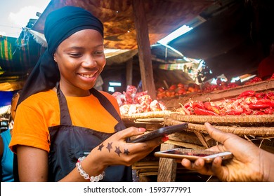 Young African Woman Selling Tomatoes In A Local African Market Receiving Payment Via Mobile Phone Transfer