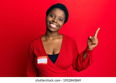 Young African Woman With Short Hair Wearing Hello My Name Is Sticker Identification Smiling Happy Pointing With Hand And Finger To The Side 