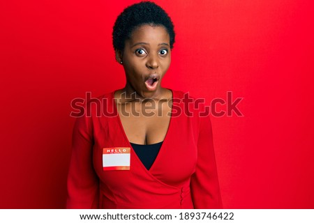 Young african woman with short hair wearing hello my name is sticker identification scared and amazed with open mouth for surprise, disbelief face 