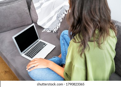 Young african woman sitting on grey couch and working at home with laptop. Safety concept.