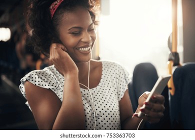 Young African woman smiling while riding on a bus listening to music on a smartphone  - Powered by Shutterstock