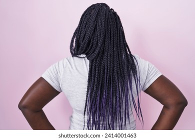 Young african woman standing over pink background standing backwards looking away with arms on body  - Powered by Shutterstock