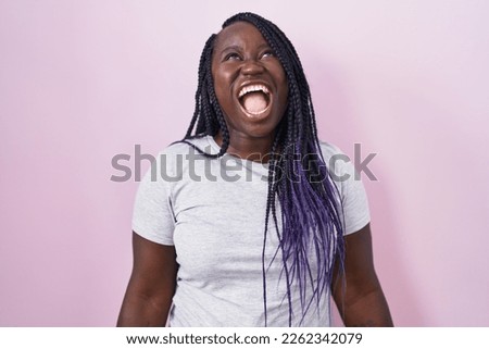Young african woman standing over pink background angry and screaming frustrated and furious, shouting with anger. rage and aggressive concept. 