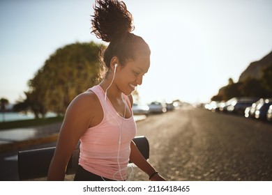 Young African woman in a tanktop and shorts smiling and listening to music on earphones while walking to yoga class
