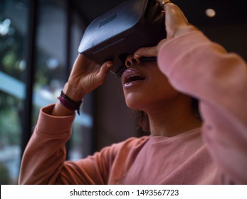 Young African woman using watching VR movie playing VR game with helmet indoor by the window happy surprised young people with Virtual technology