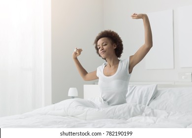 Young African Woman Waking Up Early In The Morning, She Is Sitting In Her Bed And Stretching