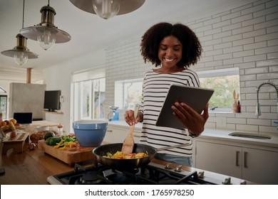 Young african woman watching recipe in digital tablet while cooking lunch in modern kitchen