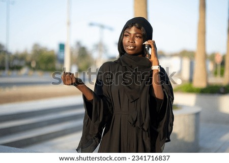 Young African woman wearing abaya talking on phone outdoors.