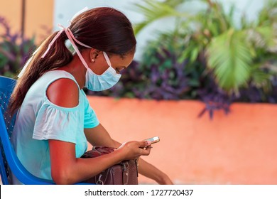 Young African woman wearing a face mask for protection and reading on her phone - concept on millennials using smartphones or devices to connect with friends, promote business and for recreation