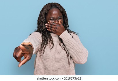 Young African Woman Wearing Wool Winter Sweater Laughing At You, Pointing Finger To The Camera With Hand Over Mouth, Shame Expression 