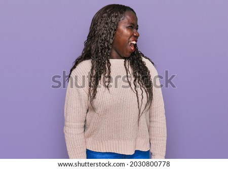 Young african woman wearing wool winter sweater angry and mad screaming frustrated and furious, shouting with anger. rage and aggressive concept. 