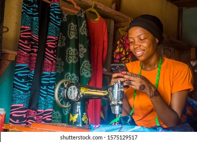 young african woman who is a tailor smiling while using her mobile phone