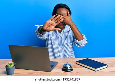 Young African Woman Working At Hotel Reception Using Laptop Covering Eyes With Hands And Doing Stop Gesture With Sad And Fear Expression. Embarrassed And Negative Concept. 