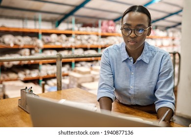 Young African Woman Working With A Laptop At Her Warehouse Desk