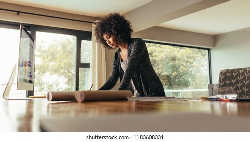 Young African Woman Working On A Building Plan On Desk. Female Architect Working At Home Office.