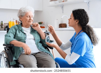 Young African-American female medical worker giving hearing aid elderly woman on wheelchair in nursing home - Powered by Shutterstock