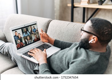 Young African-American guy relaxed lays on the couch and is talking online via video call with group of friends or employees. Black man using app on laptop for video meeting with many people together - Shutterstock ID 1752347654