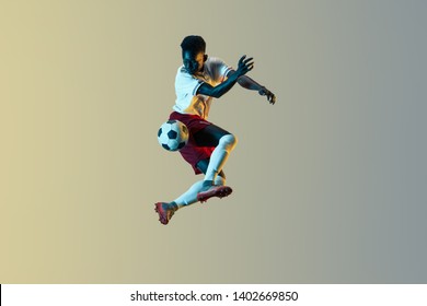 Young african-american male football or soccer player in sportwear and boots kicking ball for the goal in jump in neon light on gradient background. Concept of healthy lifestyle, professional sport. - Powered by Shutterstock