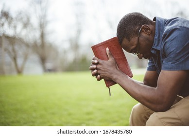 Молодой афроамериканец сидит с закрытыми глазами с Библией в руках