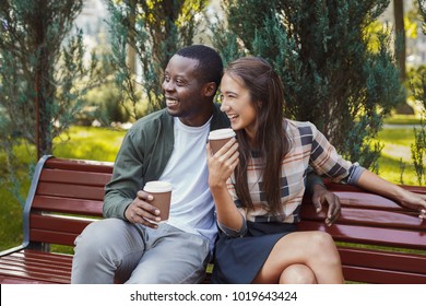 Young african-american man and asian woman sitting on bench in park and having coffee, copy space స్టాక్ ఫోటో