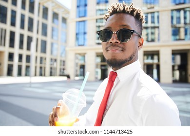 Young African-american man in formalwear and sunglassses having drink in urban environment on summer day