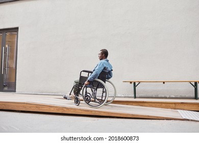 Young African-American Man With Paralyzed Legs Sitting In Wheelchair And Moving To House With Wheelchair Ramp