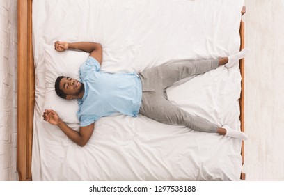 Young african-american man sleeping in bed alone, top view