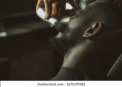 Young African-american man visiting barbershop. Brings a beard in order with the help of a hairdresser.  Self-care, masculine beauty.  Black African Hair Trimmer. - Powered by Shutterstock