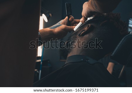Young African-american man visiting barbershop. Brings a beard in order with the help of a hairdresser.  Self-care, masculine beauty.  Black African Hair Trimmer.
