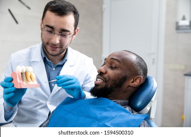 Young African-american Man Visiting Dentist's Office For Prevention And Treatment Of The Oral Cavity. Man And Male Doctor While Checkup Teeth. Healthy Lifestyle, Healthcare And Medicine Concept.