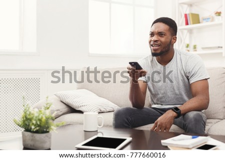 Young african-american man wathing tv. Worried guy pointing with remote controller on tv-set. Man worrying about favourite football team at home, copy space