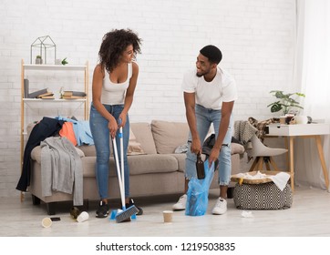 Young African-american Man And Woman Cleaning Messy Room After Party, Smiling To Each Other