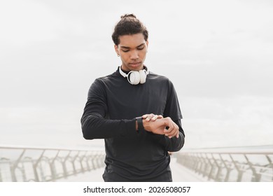 Young African-american Mixed-race Male Athlete Sportsman Checking Time On His Wrist Watch In Fitness Clothes Preparing For Jogging Running On A City Bridge In Urban Area. Active Lifestyle Concept