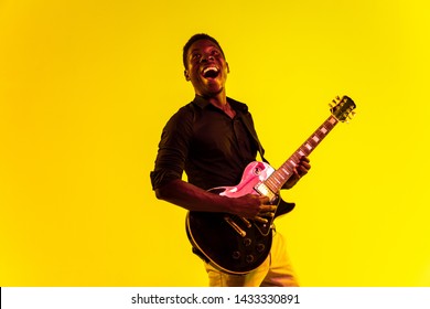 Young african-american musician playing the guitar like a rockstar on yellow background in neon light. Concept of music, hobby, festival, open-air. Joyful attractive guy improvising, singing song. - Powered by Shutterstock
